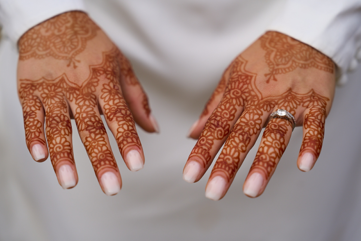 Photographe de mariage | Gros plan des mains d'une personne affichant des motifs complexes au henné, avec une bague en diamant à l'annulaire gauche.