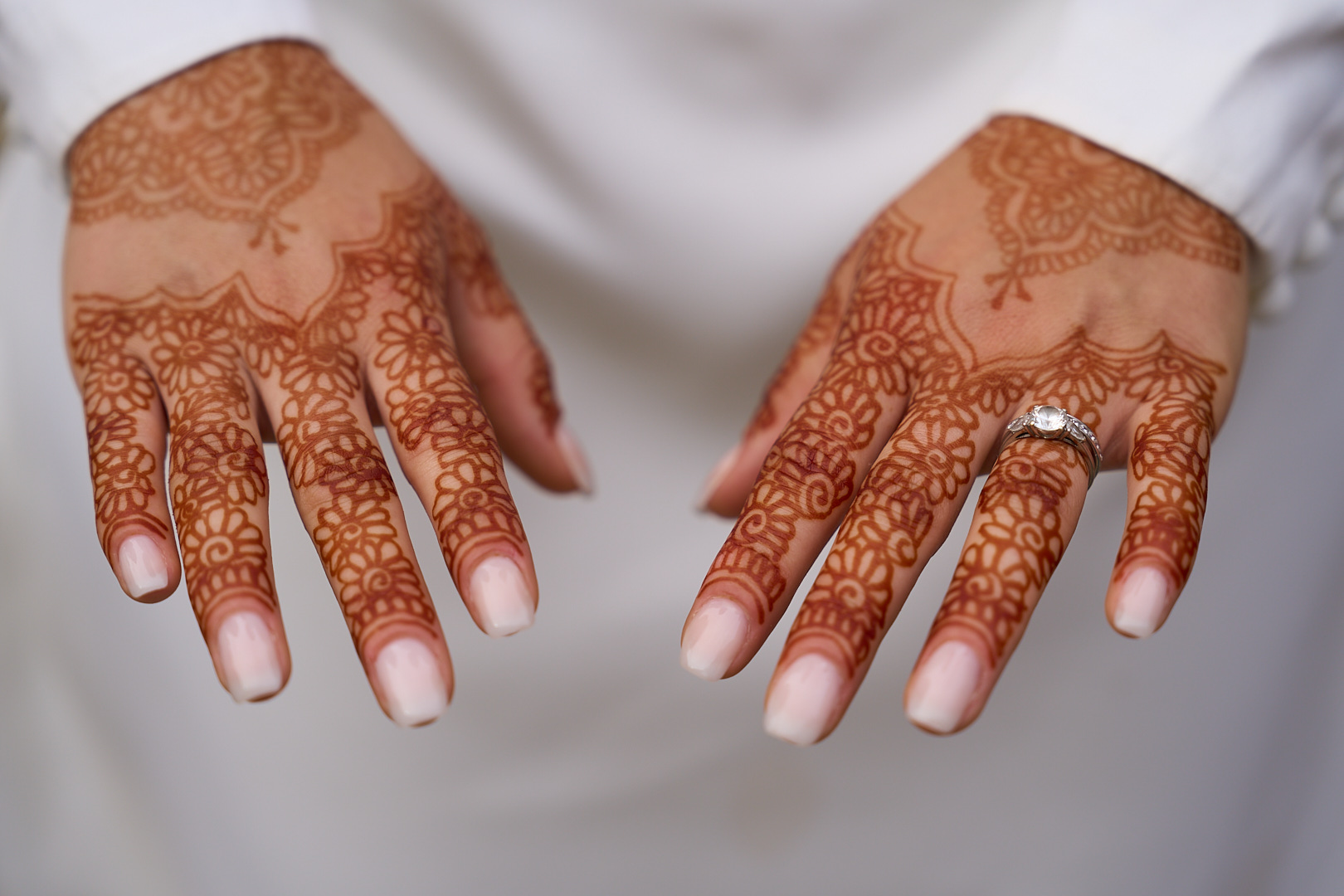 Photographe de mariage | Gros plan des mains d'une personne affichant des motifs complexes au henné, avec une bague en diamant à l'annulaire gauche.